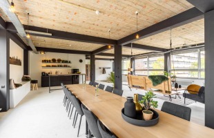 Moderne open kantoorruimte met houten plafond, lange vergadertafel en schommelbanken bij grote ramen.
