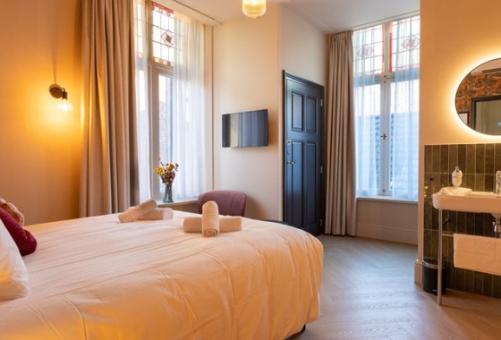 Stijlvolle hotelkamer met groot bed, moderne verlichting, dubbele ramen en wastafel met ronde spiegel.