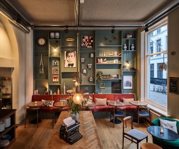 Gezellig café-interieur met rode bank, groene wandplanken, kunst en vintage typemachine op tafel.
