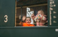 Zwei kleine Kinder winken und lächeln aus dem Fenster eines Zugabteils und schauen hinaus.
