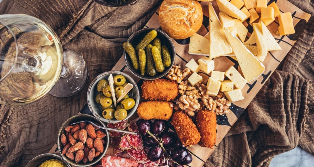 Luxe borrelplank met kaas, vleeswaren, noten, druiven, olijven, broodjes en wijn op een tafel.