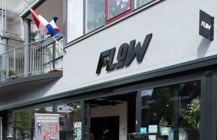 Vooraanzicht van de FLOW winkel met kleding, BMX-fietsdisplay en Nederlandse vlag op de achtergrond.