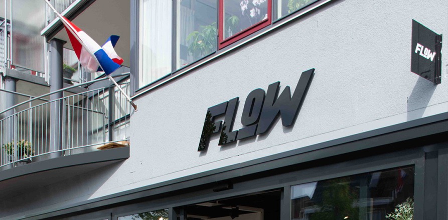 Vooraanzicht van de FLOW winkel met kleding, BMX-fietsdisplay en Nederlandse vlag op de achtergrond.
