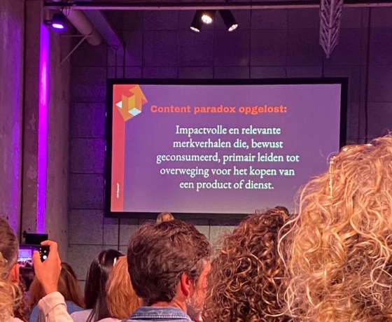 Een conferentiezaal met mensen die naar een scherm kijken waarop een presentatie over content staat.