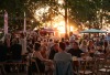 Mensen genieten van een zomers avondeten in een druk buitenrestaurant met bomen en zonsondergang.