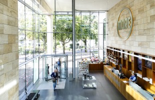 Lichte, moderne entree van het MORE museum met grote ramen, balie, bezoekers en kunstwinkel.