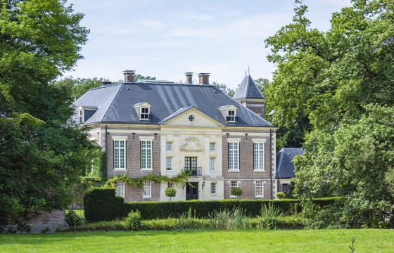 Een elegant historisch landhuis met een statige gevel, omringd door bomen en een goed onderhouden tuin.