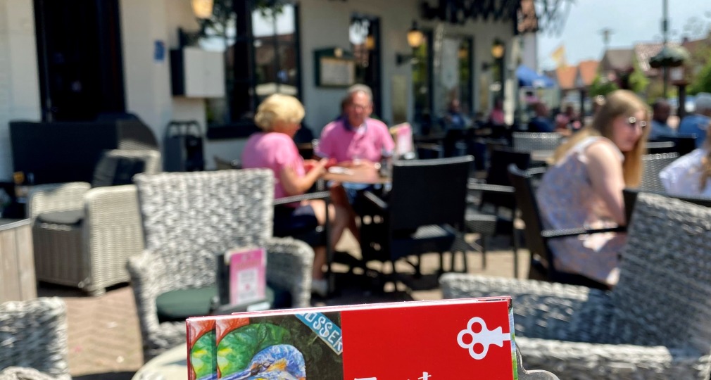 Toeristenvoordeelpas display op houten tafel bij buitenrestaurant, mensen genieten van zonnige dag.