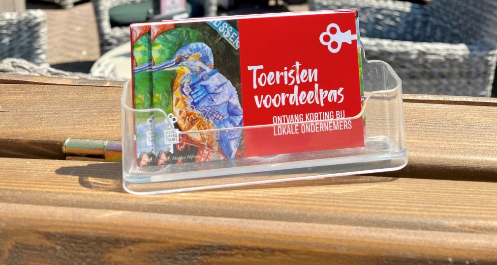 Toeristenvoordeelpas display op houten tafel bij buitenrestaurant, mensen genieten van zonnige dag.
