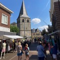 Drukke marktdag in een Nederlands stadje met mensen, marktkramen en een kerktoren op de achtergrond.