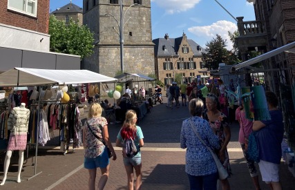 Drukke marktdag in een Nederlands stadje met mensen, marktkramen en een kerktoren op de achtergrond.