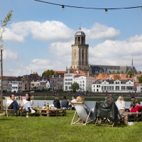 Mensen ontspannen op een grasveld met uitzicht op de IJssel en de fraaie skyline van Deventer.