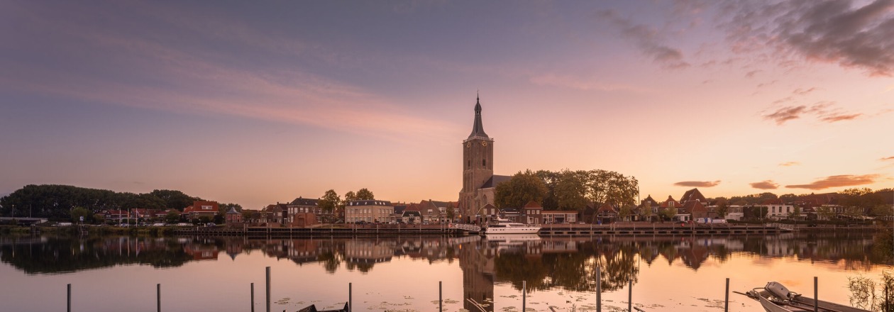 Boten liggen aan de kade bij zonsopgang met uitzicht op een kerk en historische gebouwen in Zutphen, Nederland.