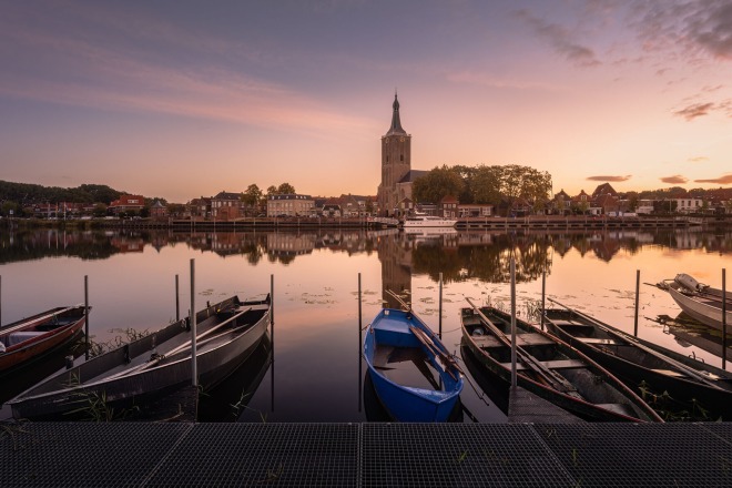 Boten liggen aan de kade bij zonsopgang met uitzicht op een kerk en historische gebouwen in Zutphen, Nederland.