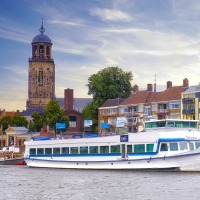 Rivierboot Nirvana vaart langs historische gebouwen en een kerktoren in een Nederlandse stad.