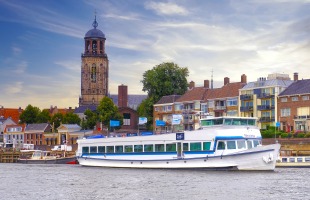 Rivierboot Nirvana vaart langs historische gebouwen en een kerktoren in een Nederlandse stad.