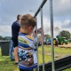 Een jongen in een New Holland-shirt maakt foto's achter een hek tijdens een tractorwedstrijd op grasveld.
