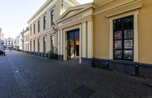 Een straat met het historische Burgerweeshuis-gebouw in Nederland, met posters bij het raam.