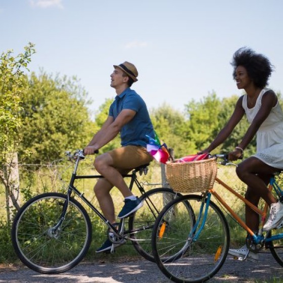 Two people riding bicycles on a sunny day along a country path, surrounded by green trees and grass.