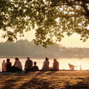 Mensen zitten en relaxen onder bomen bij een meer tijdens zonsondergang, genietend van het buitenleven.