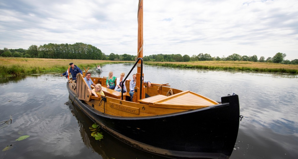 Een groep mensen geniet van een boottocht op een rustige rivier met groene oevers onder een bewolkte hemel.
