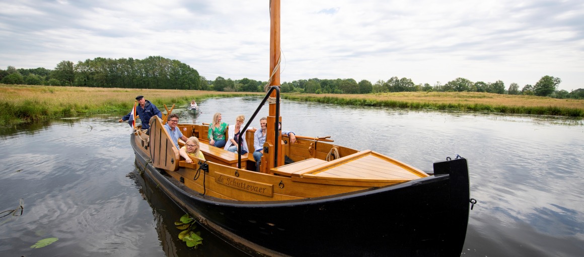 Een groep mensen geniet van een boottocht op een rustige rivier met groene oevers onder een bewolkte hemel.