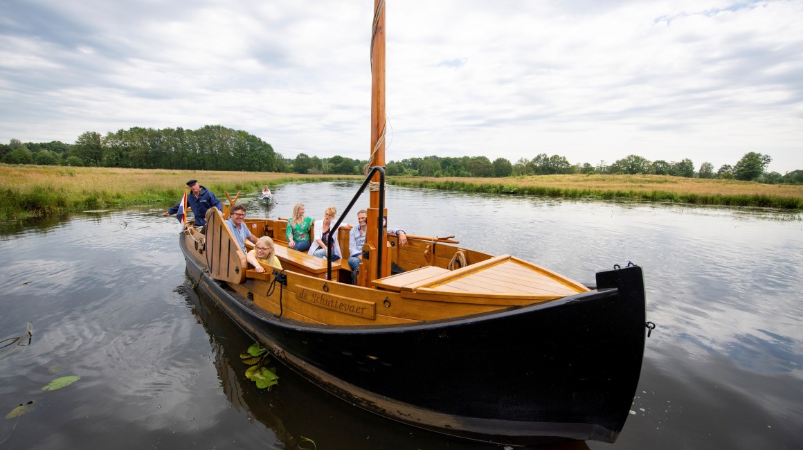 Een groep mensen geniet van een boottocht op een rustige rivier met groene oevers onder een bewolkte hemel.