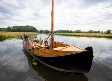 Een groep mensen geniet van een boottocht op een rustige rivier met groene oevers onder een bewolkte hemel.