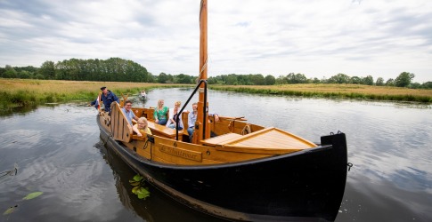 Een groep mensen geniet van een boottocht op een rustige rivier met groene oevers onder een bewolkte hemel.