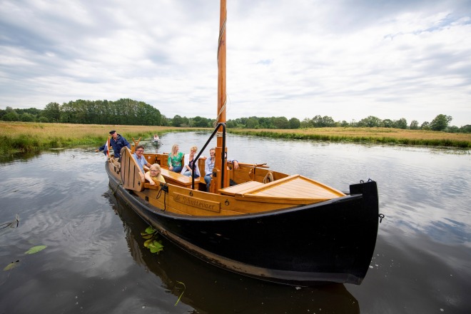 Een groep mensen geniet van een boottocht op een rustige rivier met groene oevers onder een bewolkte hemel.
