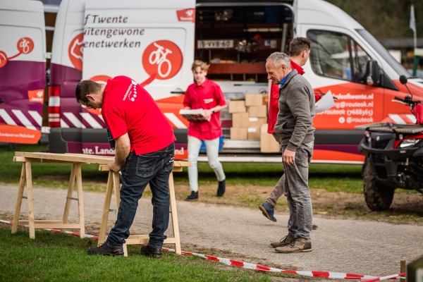 Mensen zijn buiten aan het werk met gereedschap en materialen voor een bestelbus met oranje bestickering.