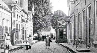 Zwart-witfoto van de Heerenstraat in Raalte met mensen en kindergezichten, oude bakstenen gebouwen.