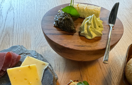 Een gourmetselectie met kaas, vleeswaren, gefrituurde balletjes en dips op een houten tafel.