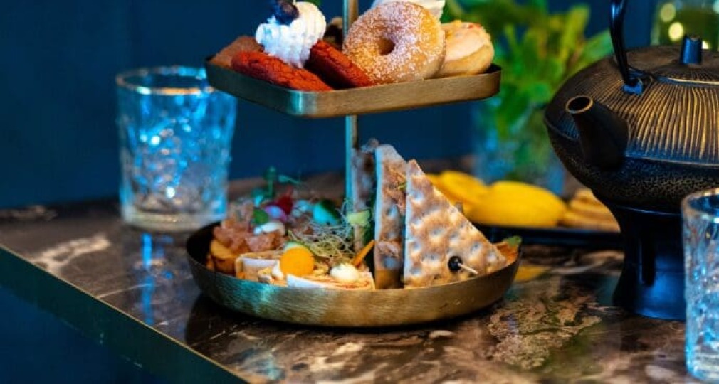 Trapsgewijze serveerschaal met luxe zoete en hartige hapjes, glazen en een theepot op een marmeren tafel.