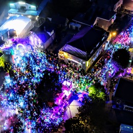Luchtfoto van een nachtelijk festival met kleurrijke verlichting en een grote menigte in een stadscentrum.