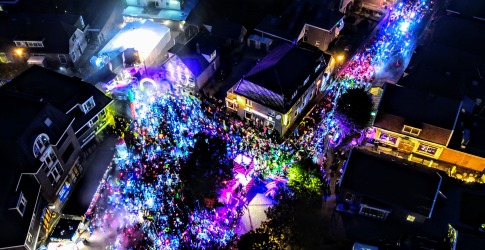 Luchtfoto van een nachtelijk festival met kleurrijke verlichting en een grote menigte in een stadscentrum.