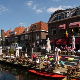 Terras aan het water in een Nederlands stadje met mensen die genieten van het zonnige weer.