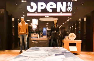 Een kledingwinkel met jeansdisplay, mannequins en een groot 'OPEN 32' bord op de achtergrond.