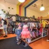 Zwei Frauen sortieren Kinderkleidung in einem farbenfrohen Geschäft mit Jacken, Kleidern und Schuhen.