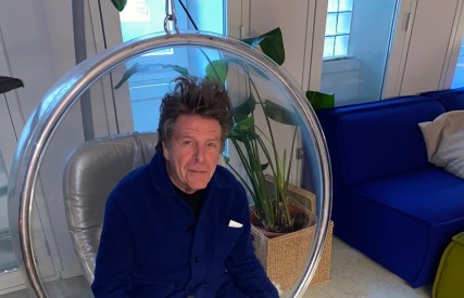 Man zit ontspannen in een ronde, hangende stoel in een moderne kamer met planten en een blauwe bank.