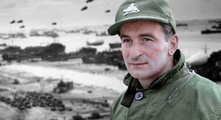 Een gekleurde soldaat in uniform met een groene pet op het strand tijdens de Tweede Wereldoorlog.