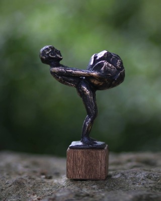 Bronzene Miniaturfigur einer Person, die einen großen Kohlkopf hält, auf einem hölzernen Sockel stehend.