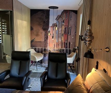 Een moderne woonkamer met zwarte stoelen en een trompe-l'oeil muurschildering van een straatje.