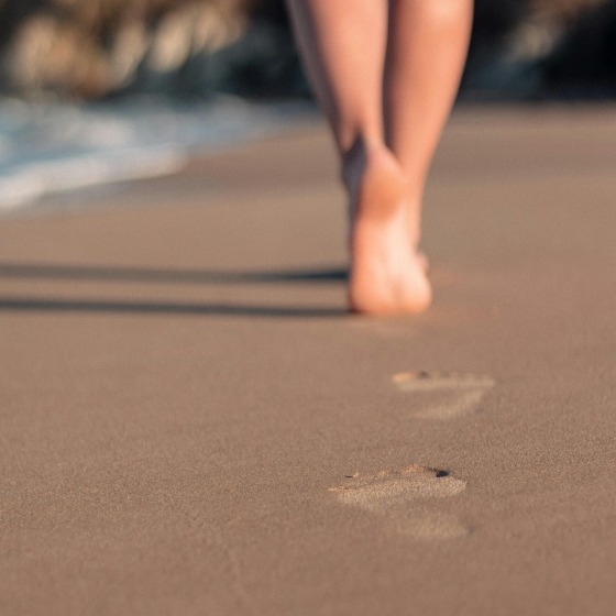 Voetafdrukken op het zand terwijl een persoon blootsvoets over het strand langs de kustlijn loopt.