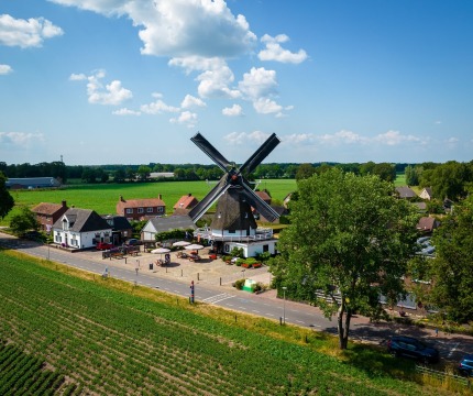Traditionele Nederlandse windmolen omringd door groene velden en huizen in een landelijk landschap.