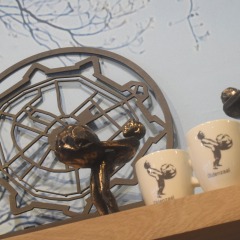 Figuren und Tassen mit einer Skulptur einer Person, die eine Kugel trägt, auf einem Holzregal ausgestellt.