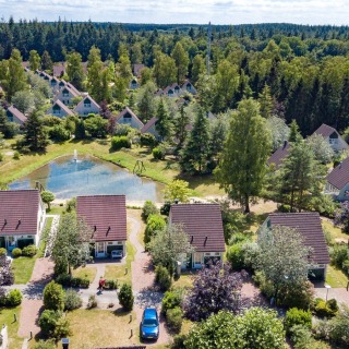 Luchtfoto van een vakantiepark in een bosrijk gebied met huisjes, vijver en veel groene bomen.