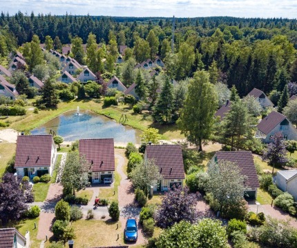 Luchtfoto van een vakantiepark in een bosrijk gebied met huisjes, vijver en veel groene bomen.