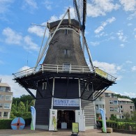 Historische Nederlandse windmolen met kunsttentoonstelling, blauwe lucht en omliggende moderne gebouwen.