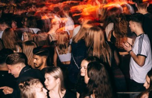 Een menigte jonge mensen in een nachtclub onder kleurrijke lichten, met beweging en energie overal.